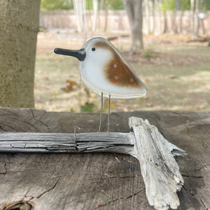 fused glass brown and white speckled sandpiper bird ornament perched on driftwood and resting on a log in woodland garden