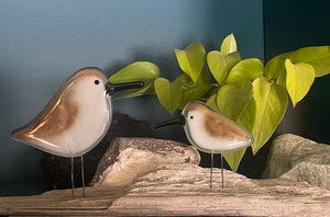 Two glass sandpiper birds on a wooden surface with green leaves in the background