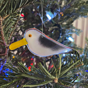 Glass bird ornament hanging on a Christmas tree with blurred lights in the background