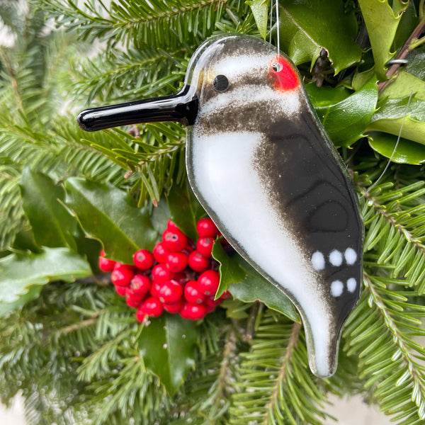 Load image into Gallery viewer, a black and white fused glass hairy woodpecker hangs in front of a holly-laden wreath
