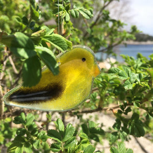 A glass goldfinch hanging in a Rose Bush