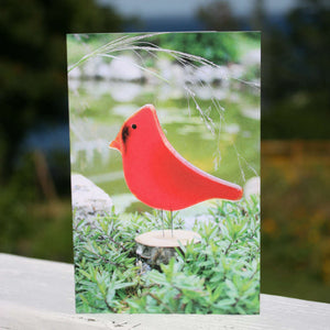 A greetings cards featuring a red glass cardinal amongst the creeping thyme. A pond is in the background.