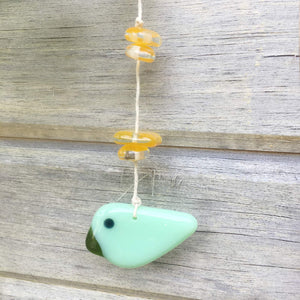 Small green glass bird hanging from a string, accented with yellow beads