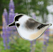 Load image into Gallery viewer, A black, grey and white glass chickadee hanging ornament against a backdrop of purple lupins

