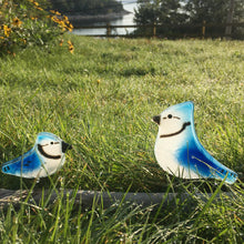 Load image into Gallery viewer, Two glass bluejays (a chick and adult) perch facing each other on a piece of driftwood in some long grass on a summers evening
