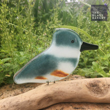Load image into Gallery viewer, Teal Blue, white and rust coloured glass Kingfisher bird ornament perched on driftwood against a background of green foliage.
