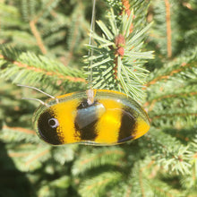Load image into Gallery viewer, A small gold and black fused glass bee hangs in front of an evergreen tree
