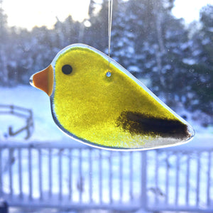 A glossy black and yellow female goldfinch hanging ornament dangles in front of a snowy scene
