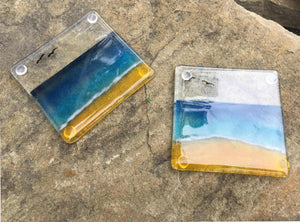 Two glass coasters featuring a blue, aqua and sandy coloured beach scene.