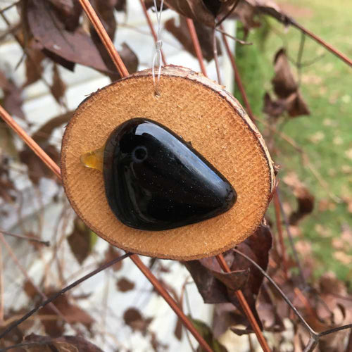 A small black glossy glass bird mounted on a slice of log - hanging ornament