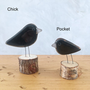 Two black glass crows of different sizes sit on log perches on a wooden table.