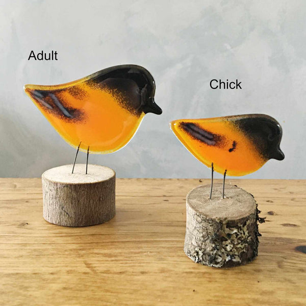 Charger l&#39;image dans la galerie, A small and large glass orange oriole bird sit on logs. The birds sit on a table.
