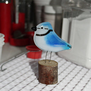 Charming Glass Blue Jay chick on a log. Workshop in the background.