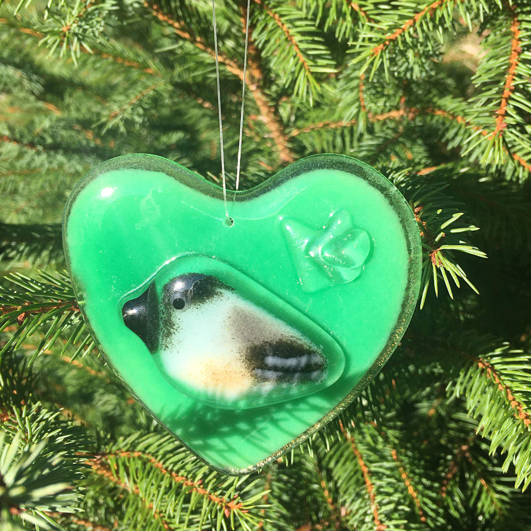 A Green Fused Glass Heart with Chickadee hangs in front of a Christmas Tree