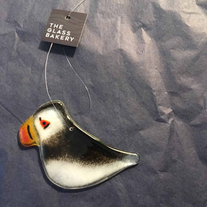 A glossy black and white bird with orange beak. This  is a hanging puffin ornament and is placed on a blue background of tissue paper