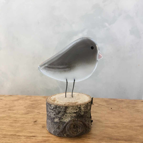 A grey and white glass bird ornament with a pink beak (Dark Eyed Junco).