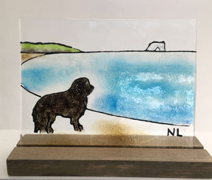 A fused glass panel. A black Newfoundland dog looks out over the ocean. There's an iceberg in the background .