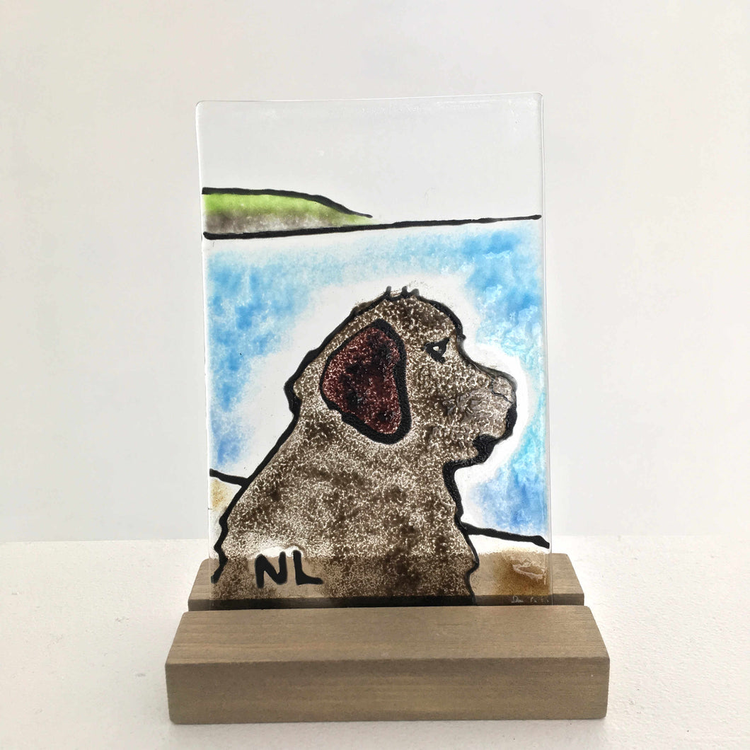 A studio-glass tile featuring a side profile of a Newfoundland dog gazing out to sea. The glass tile is in a wood stand.