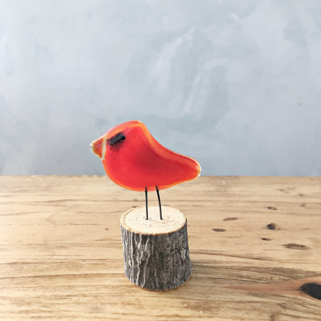 A mini red glass cardinal bird ornament is perched on a small live edge log on a table