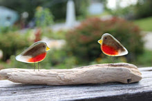 Load image into Gallery viewer, In the foreground are two brown and red glass robin bird ornaments perched on a driftwood log. The background is out of focus but a garden scene.
