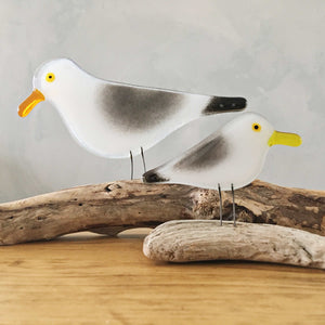 Two glass bird ornaments (grey, black and white with gold beaks), modelled to look like seagulls .