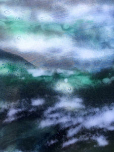 Close up photo of a glass landscape powder painting in various shades of greens, blues and browns.