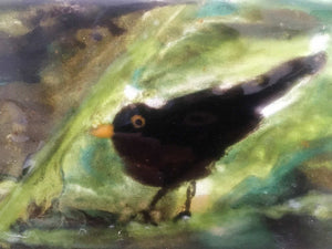 close up of a glass tile featuring a blackbird in a bush