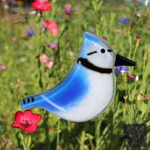 Load image into Gallery viewer, A glass bluejay ornament hangs in front of red and purple wildflowers
