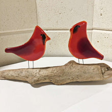 Load image into Gallery viewer, A pair of glass red birds on driftwood. The photo is taken with the walls of a glass kiln in the background
