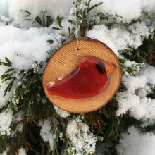 Load image into Gallery viewer, a small red glass cardinal bird has been mounted on a log and thread as a hanging ornament. Photo taken against a backdrop of snowy trees
