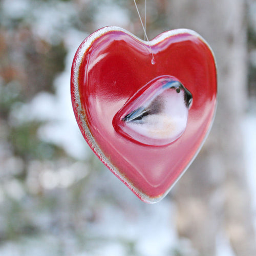 A smooth glossy red glass heart with a chickadee bird on the front