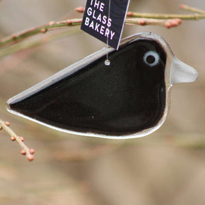 A glossy black hanging crow ornament with a grey beak. The bird hangs from a branch with red berries