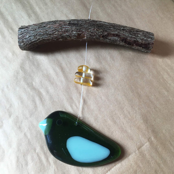 Load image into Gallery viewer, a two toned fused glass green Bird hangs from driftwood and is accented by yellow beads.
