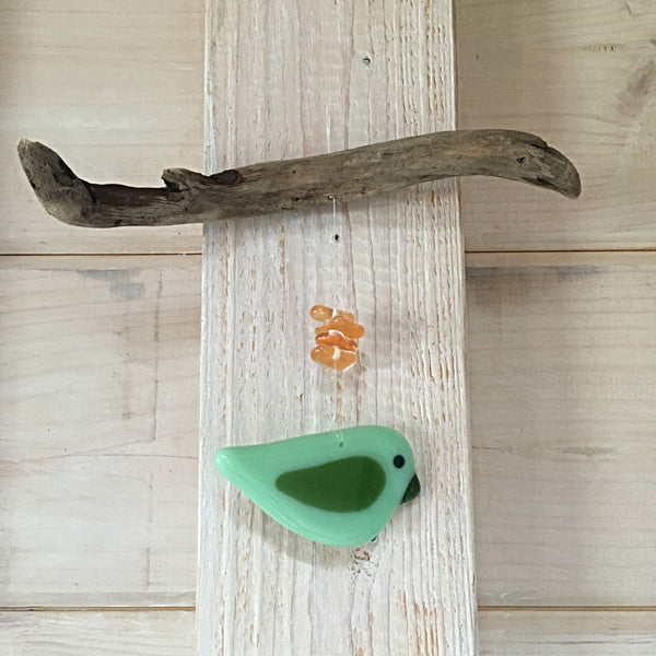 Load image into Gallery viewer, a two toned fused glass green Bird hangs from driftwood and is accented by orange glass beads

