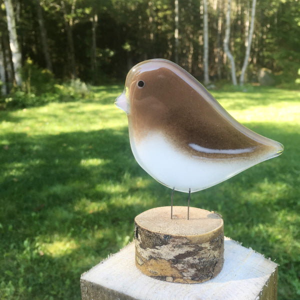 Load image into Gallery viewer, Brown and white glass bird ornament with pink beak. The bird sits on a slice of log for a perch and the backdrop is a green wooded landscape
