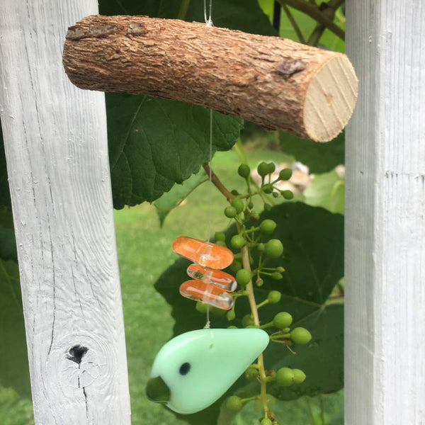 Load image into Gallery viewer, a two toned fused glass green Bird hangs from driftwood and is accented by orange glass beads
