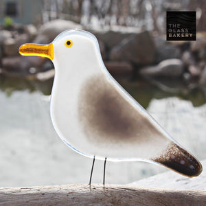 glass seagull with orange beak sits next to a pond